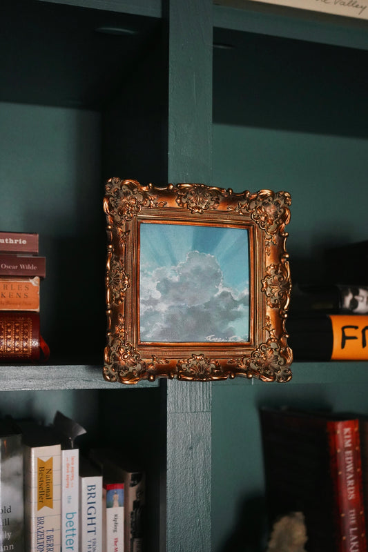 painting of clouds with silver lining set in ornate gold frame hung on built-in bookshelves